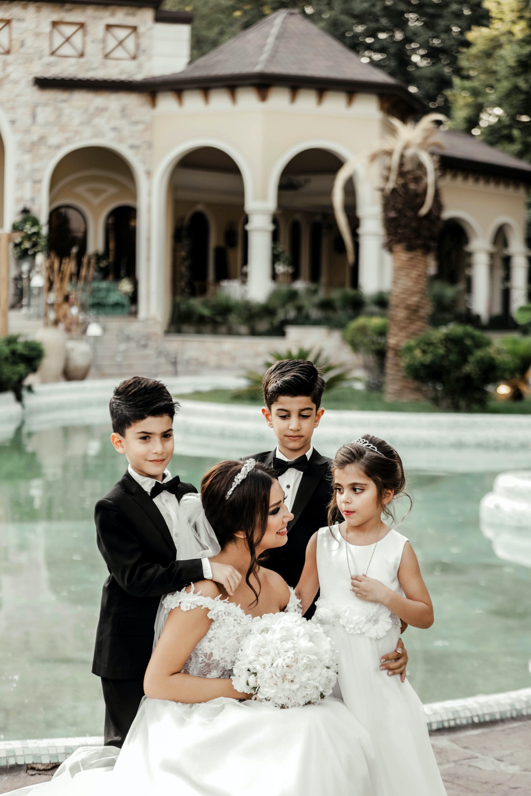 Elegant wedding family portrait with bride and children by fountain in luxury outdoor venue romantic fine art wedding photography