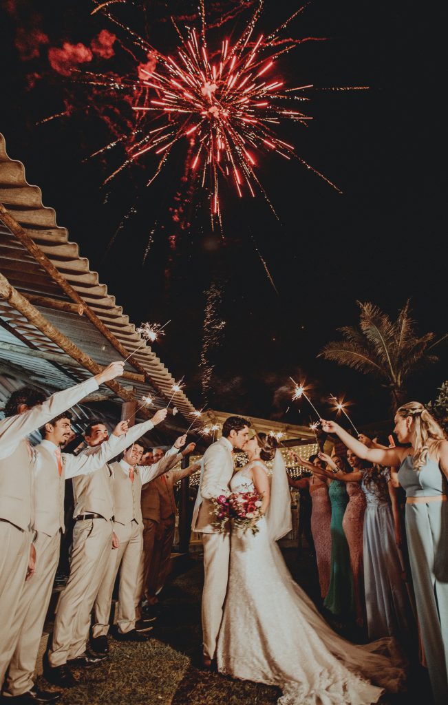 Wedding couple kissing under fireworks with guests holding sparklers at outdoor reception