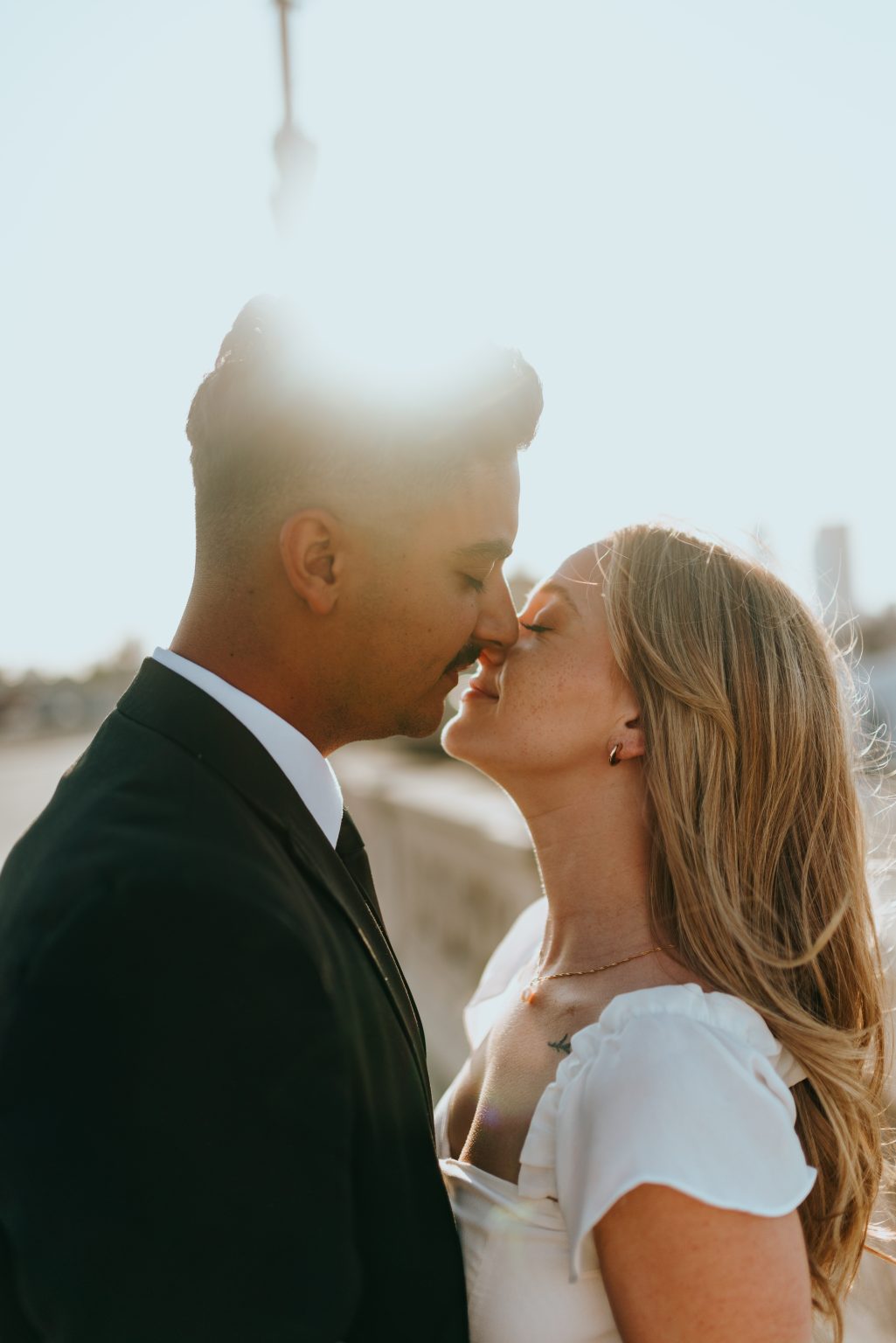 Romantic sunset wedding couple portrait with bride and groom sharing intimate kiss in warm golden light outdoors