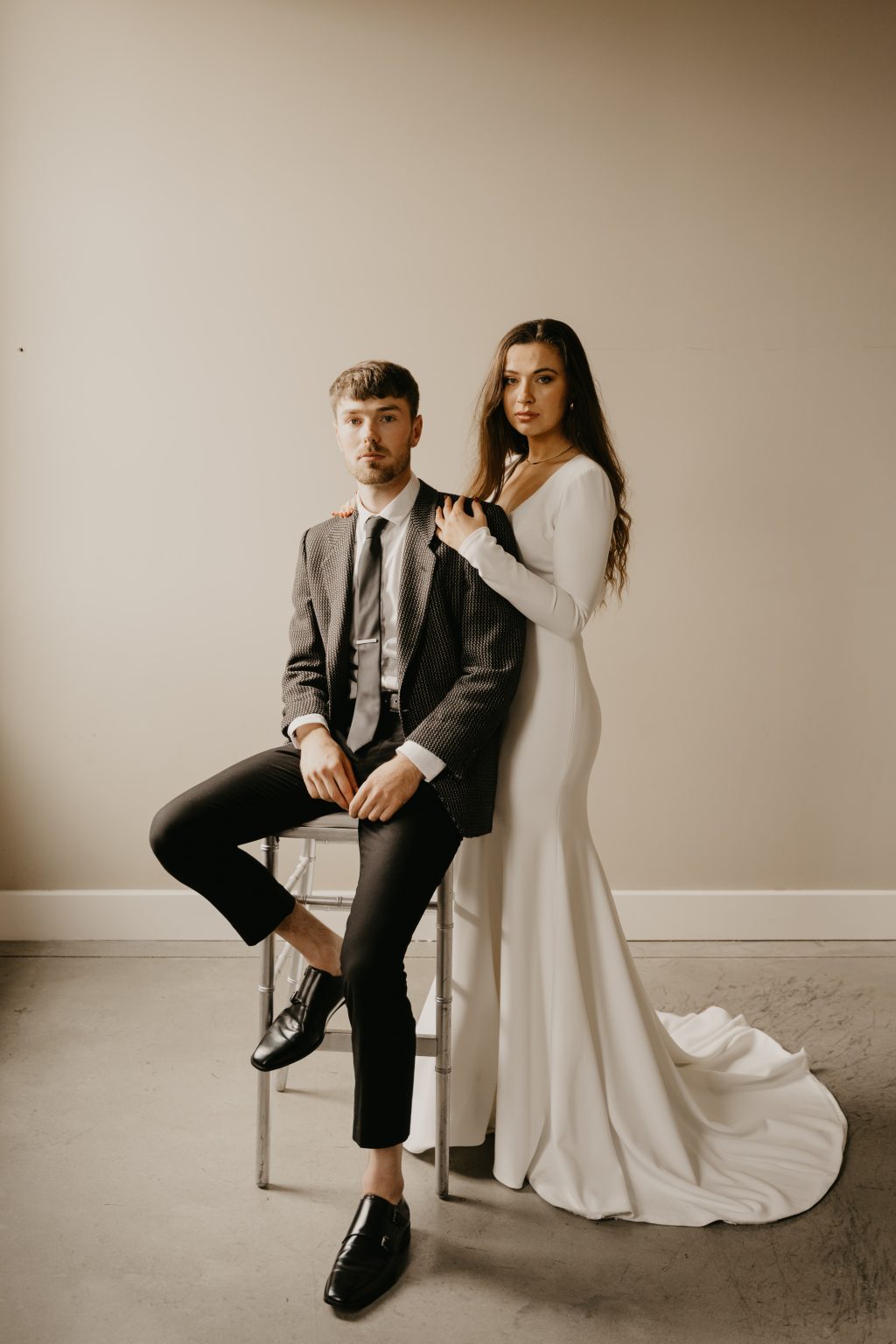 Minimalist wedding couple portrait with bride in elegant white gown and groom in modern suit against neutral background