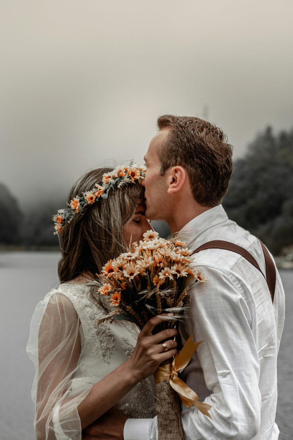 Outdoor wedding couple embracing by a lake with bouquet in scenic destination setting