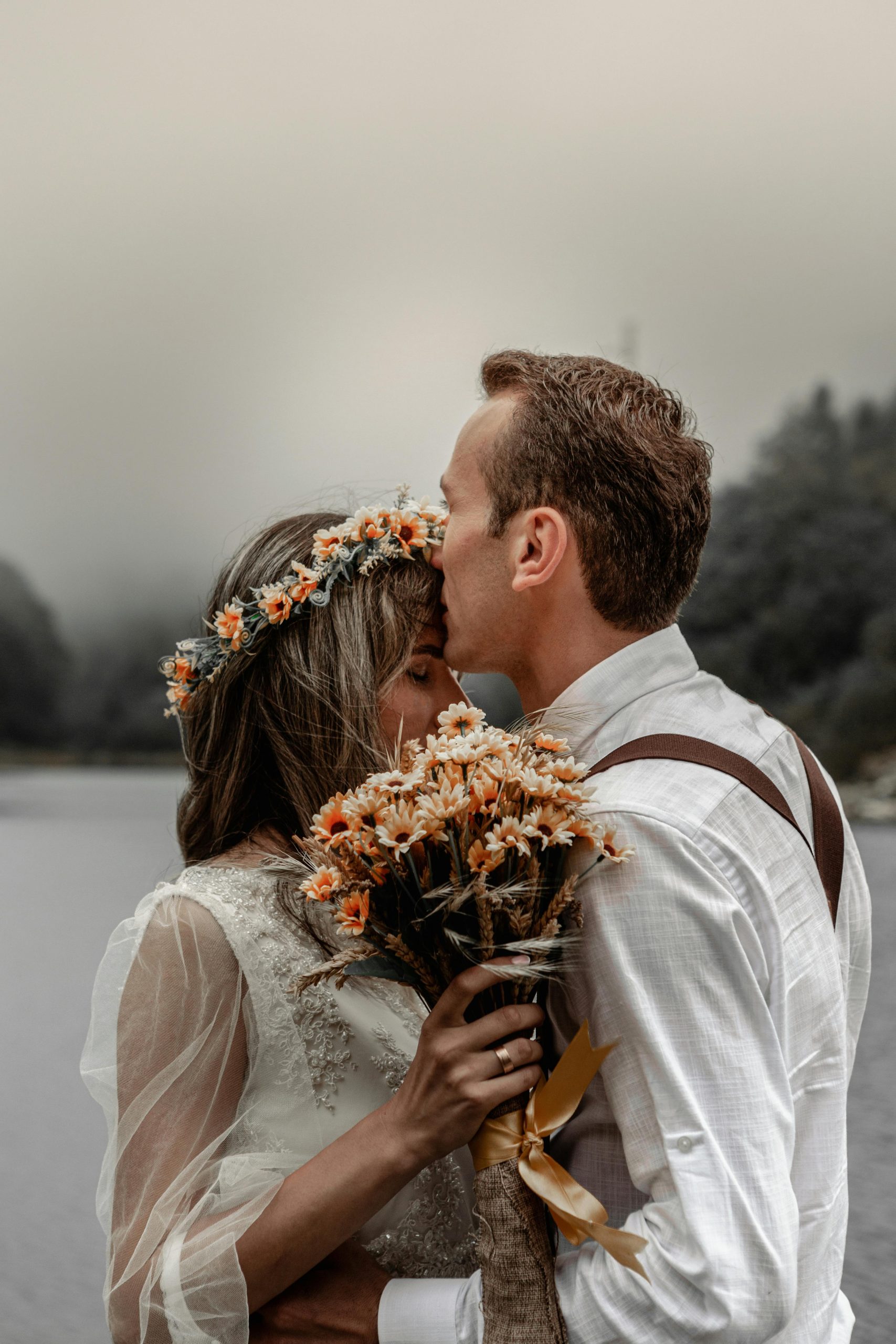 Outdoor wedding couple embracing by a lake with bouquet in scenic destination setting
