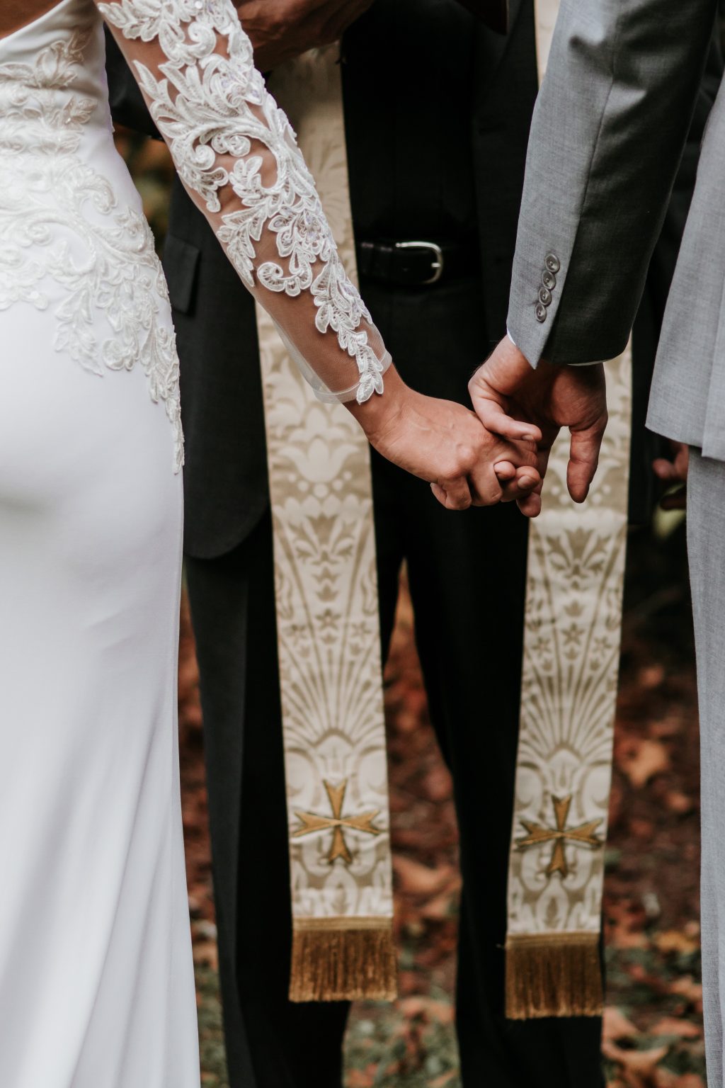 Wedding ceremony detail of couple holding hands with lace dress and priest stole